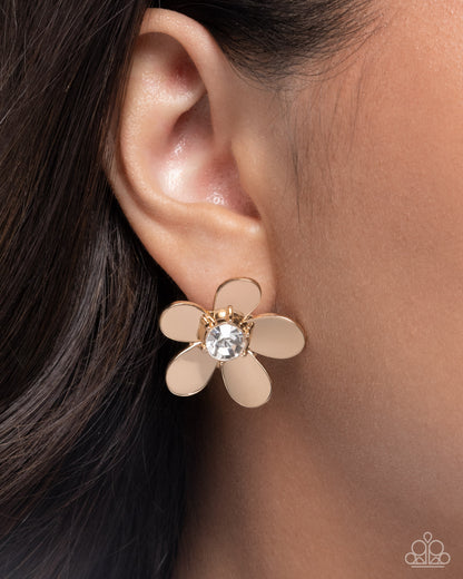 Gold flower-shaped earring with a central gemstone worn by a person.