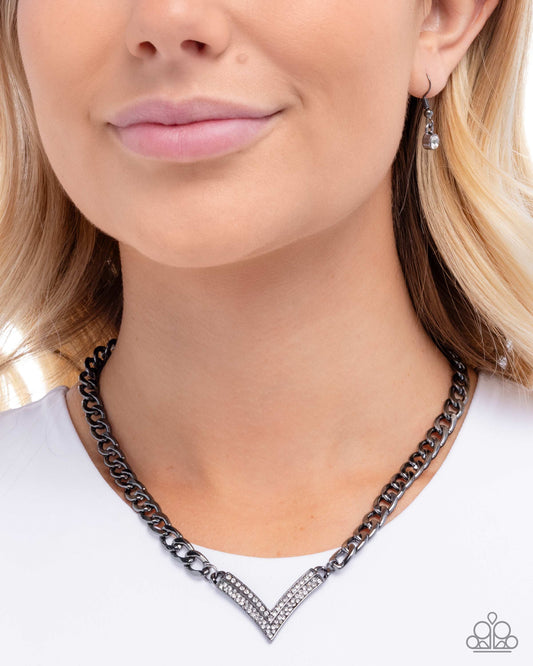Necklace with black chain and clear stones worn by a person on a white background