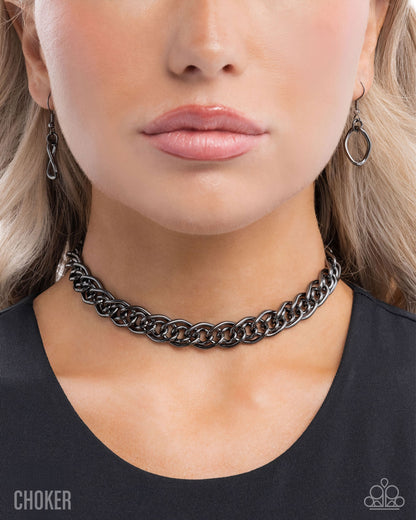 Close-up of a person wearing a black chain choker necklace and earrings.