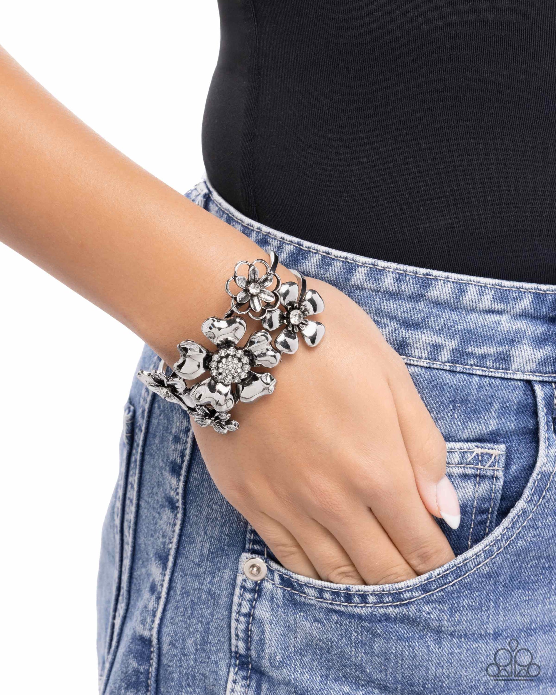 Silver floral bracelet on a wrist with a black top and blue jeans.