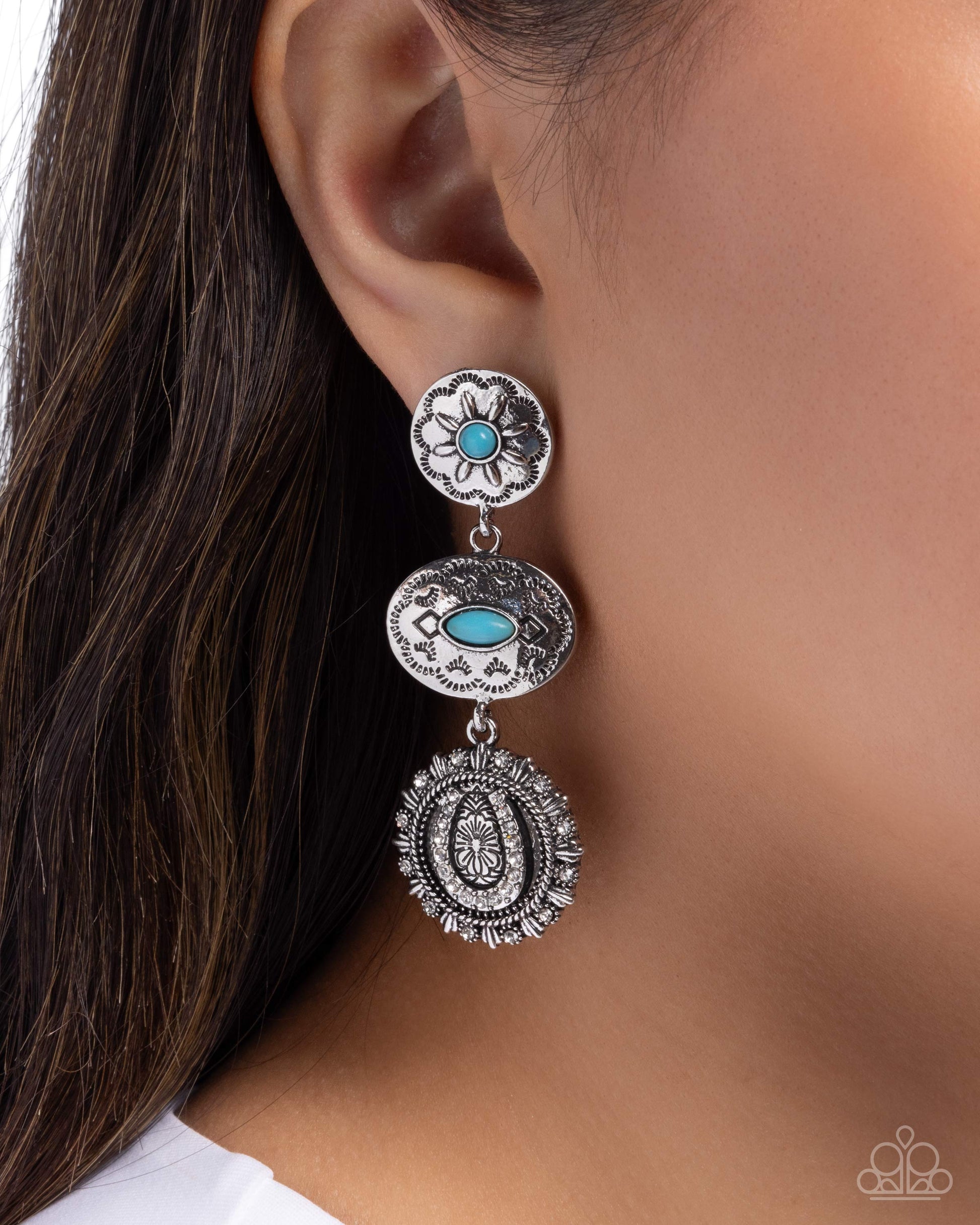 A close-up of a model's ear wearing a three-tiered silver dangle earring with turquoise blue stone accents.
