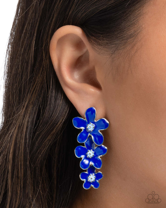 Blue floral earring worn on an ear with dark hair and skin background