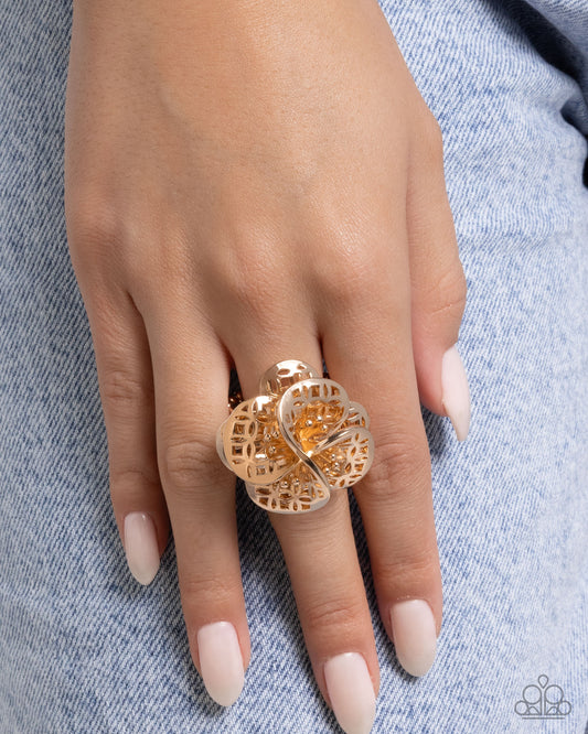 Gold ring on a hand with light pink nail polish against a denim background