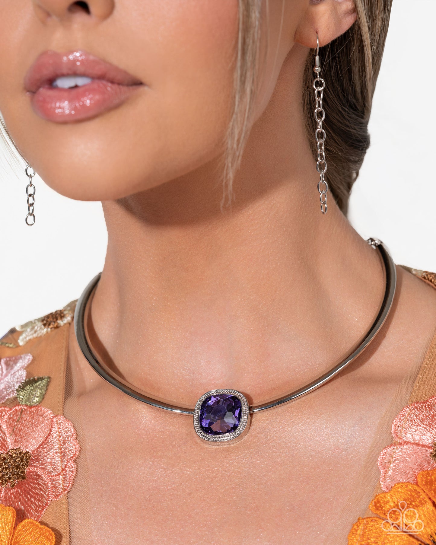 Close-up of a woman wearing a silver necklace with a purple gemstone and matching earrings.