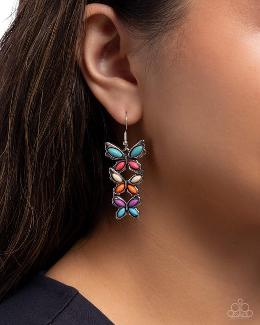 Multicolored butterfly earrings worn by a person with dark hair.