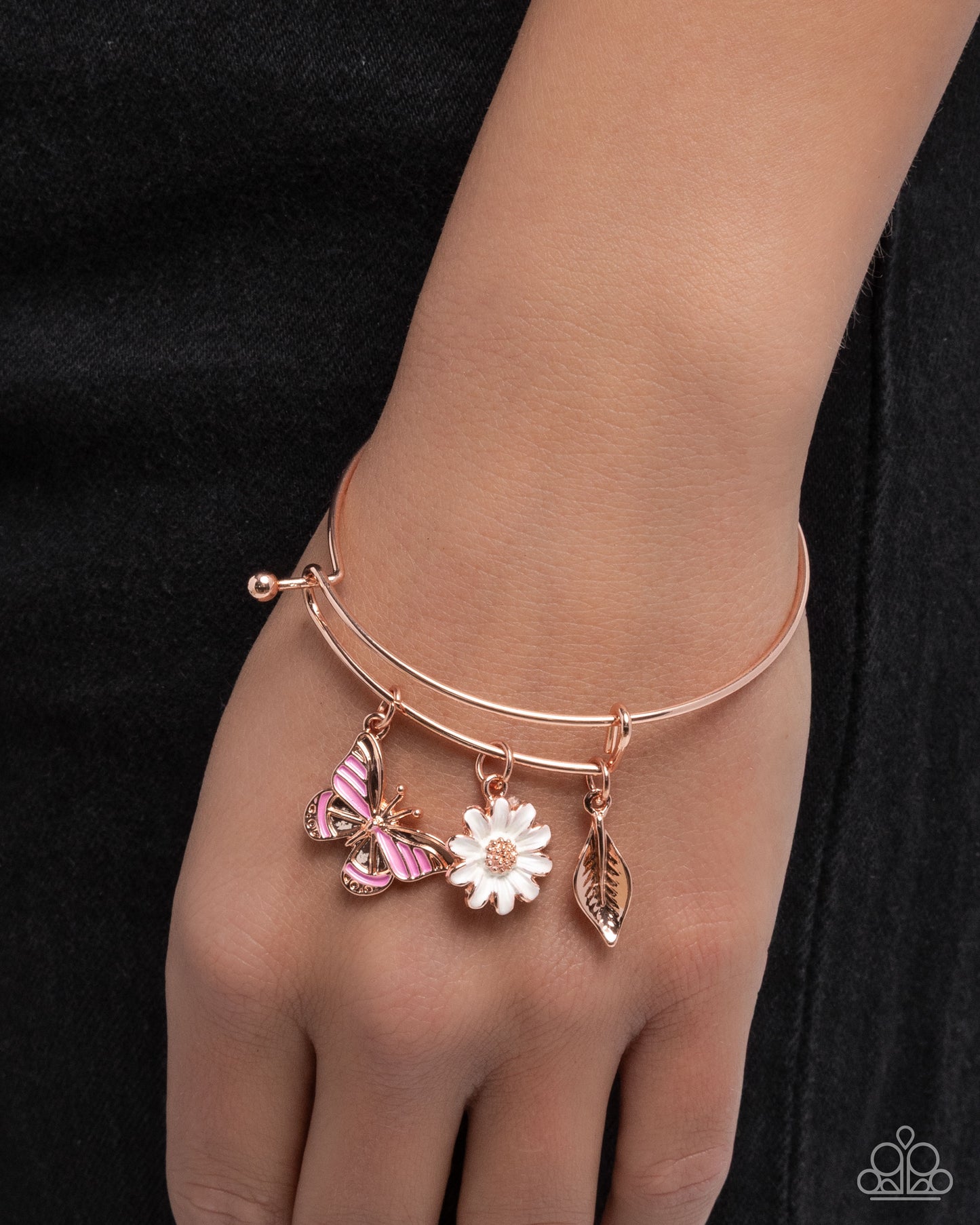 Rose gold bracelet with floral and butterfly charms on a wrist against a black background