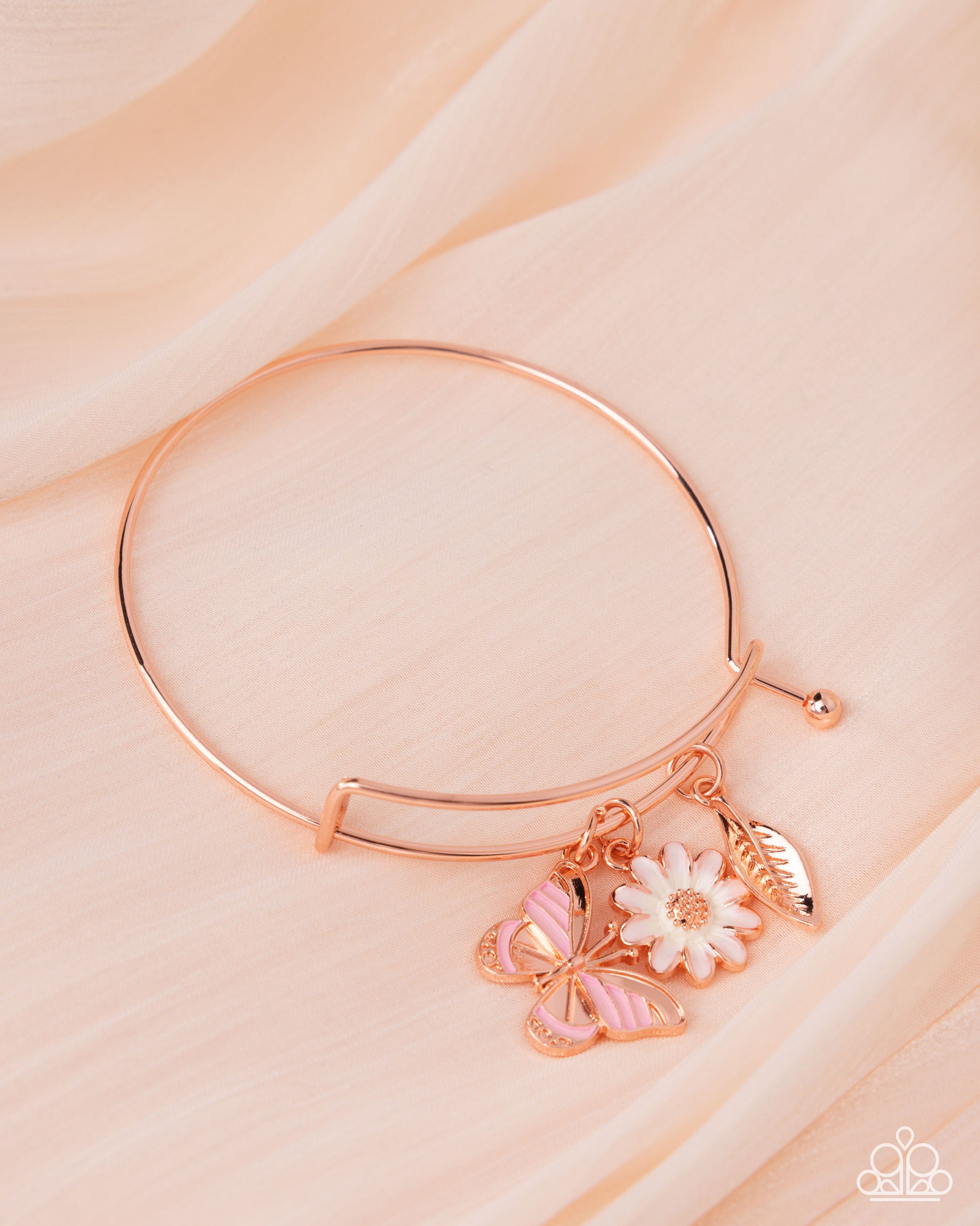 Rose gold bracelet with butterfly and flower charms on a light pink background