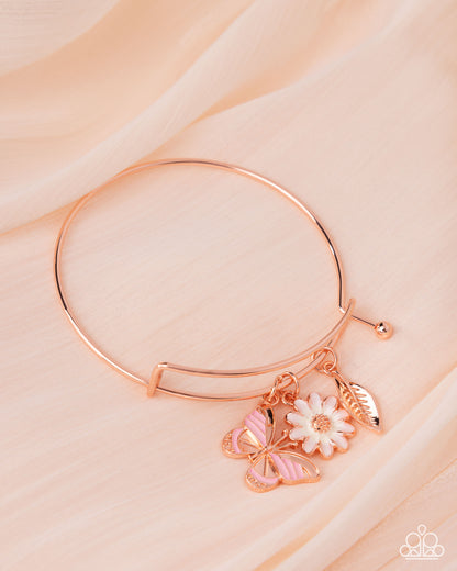 Rose gold bracelet with butterfly and flower charms on a light pink background