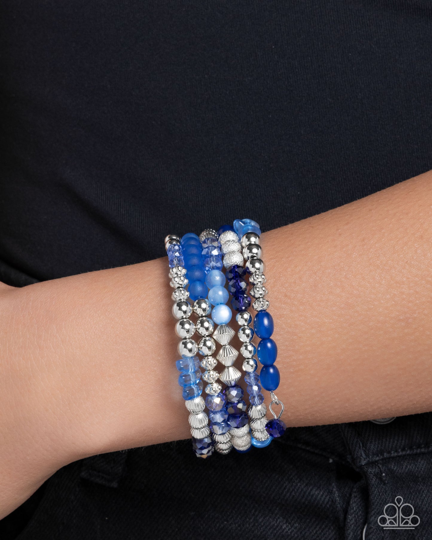 Stack of blue beaded bracelets on a wrist against a black background