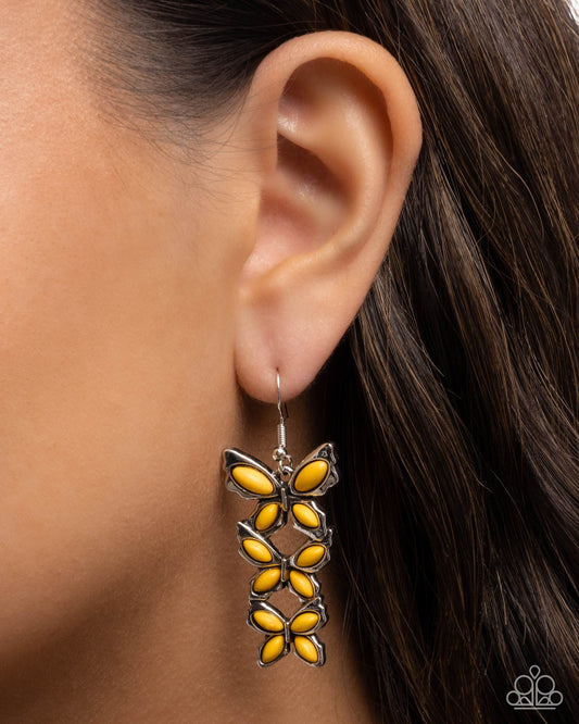 Yellow butterfly earrings worn by a model with dark hair.