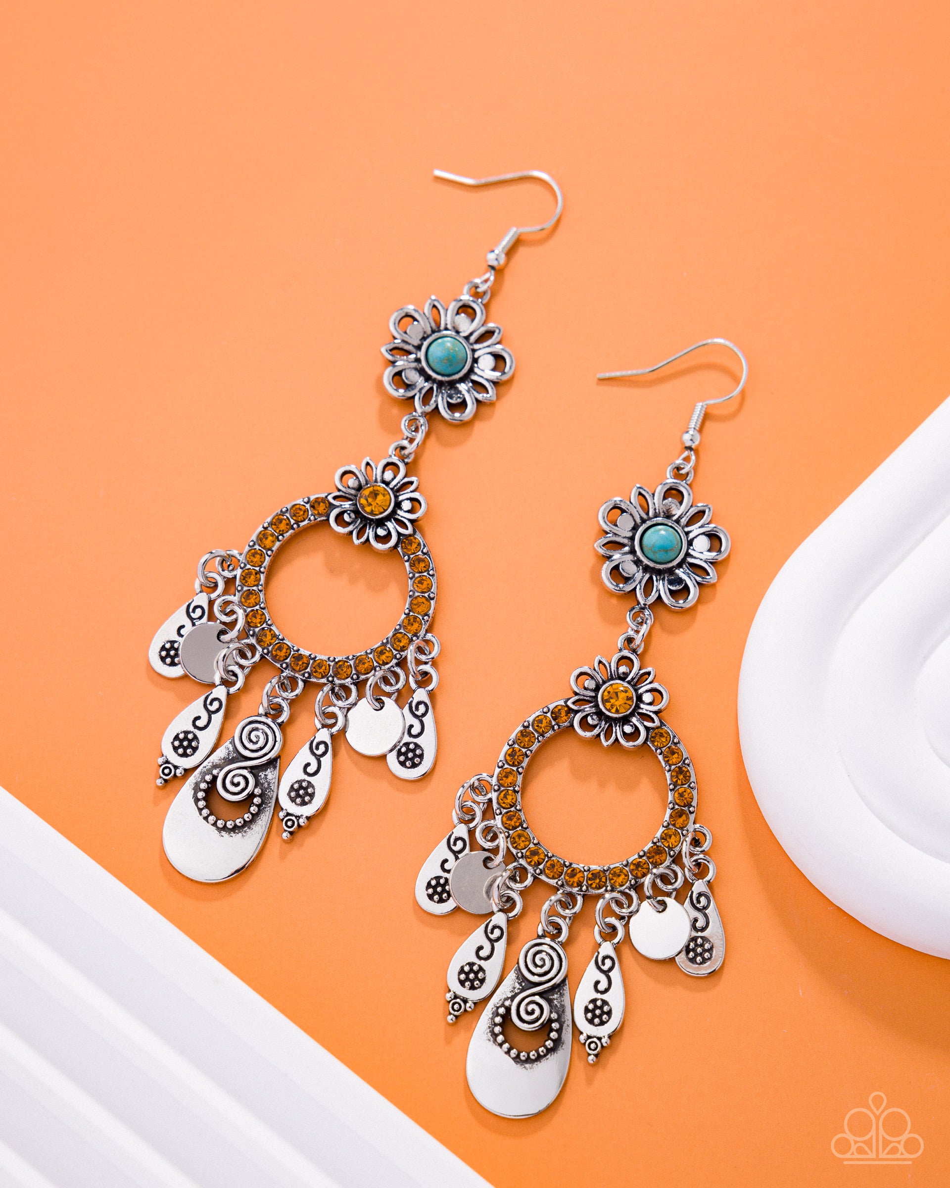 Pair of silver and turquoise floral earrings on an orange background