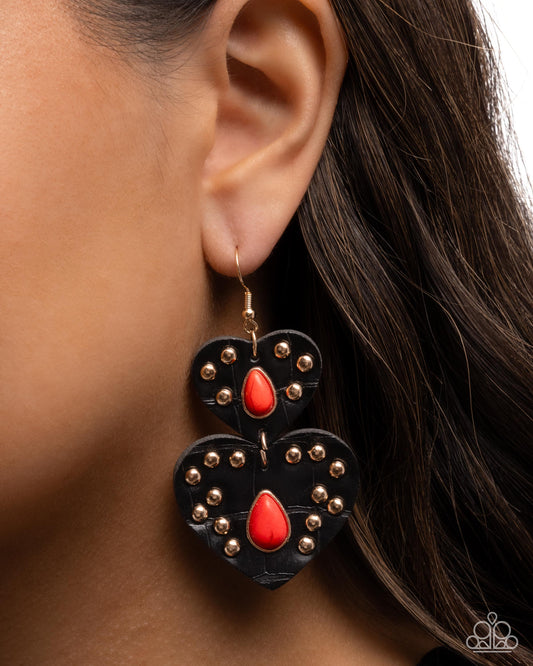 Black heart-shaped earrings with red teardrop designs and gold studs worn by a person.