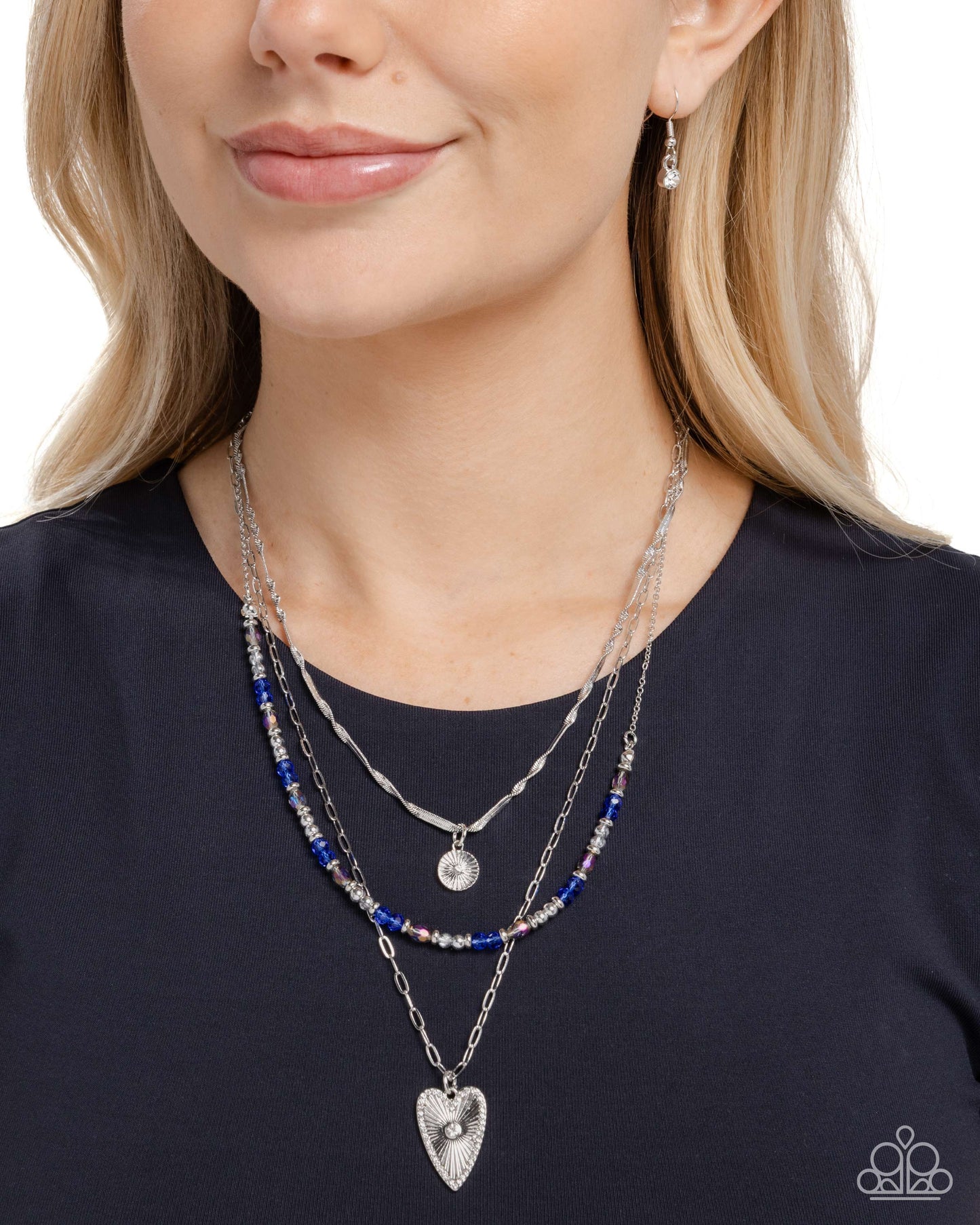 Woman wearing a layered necklace with blue beads and silver heart pendant on a plain background