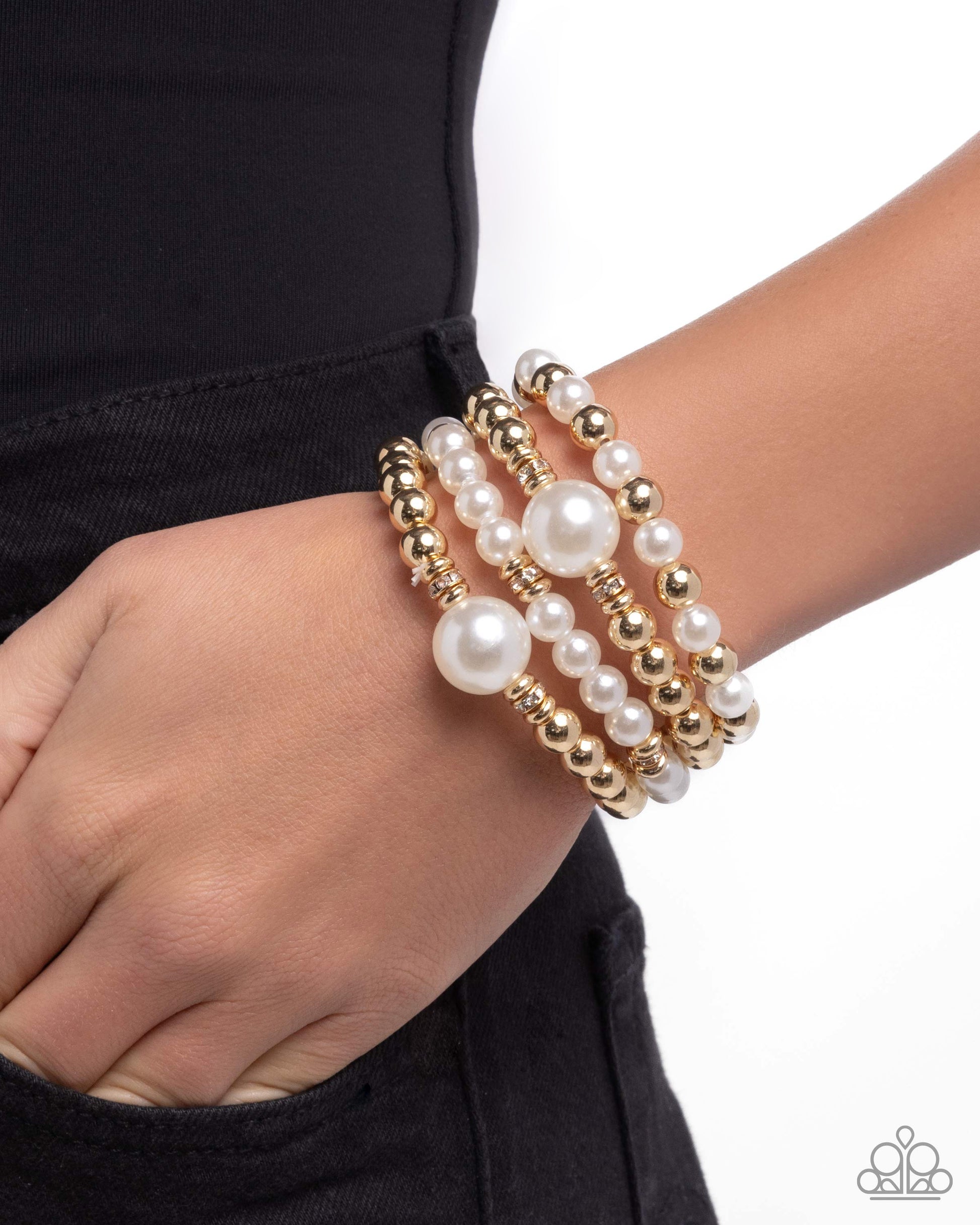 Three pearl and gold beaded bracelets on a wrist against a black background
