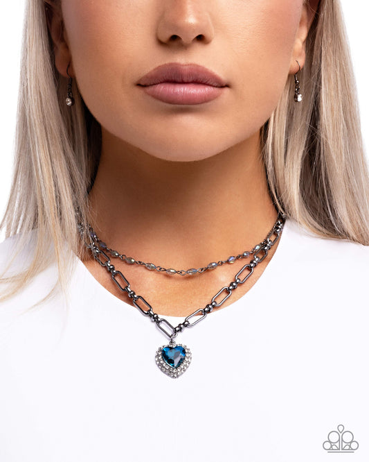 Necklace with heart-shaped blue gemstone pendant worn by a model on a white background