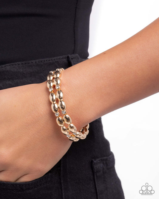 Gold bracelet on a wrist with a plain background