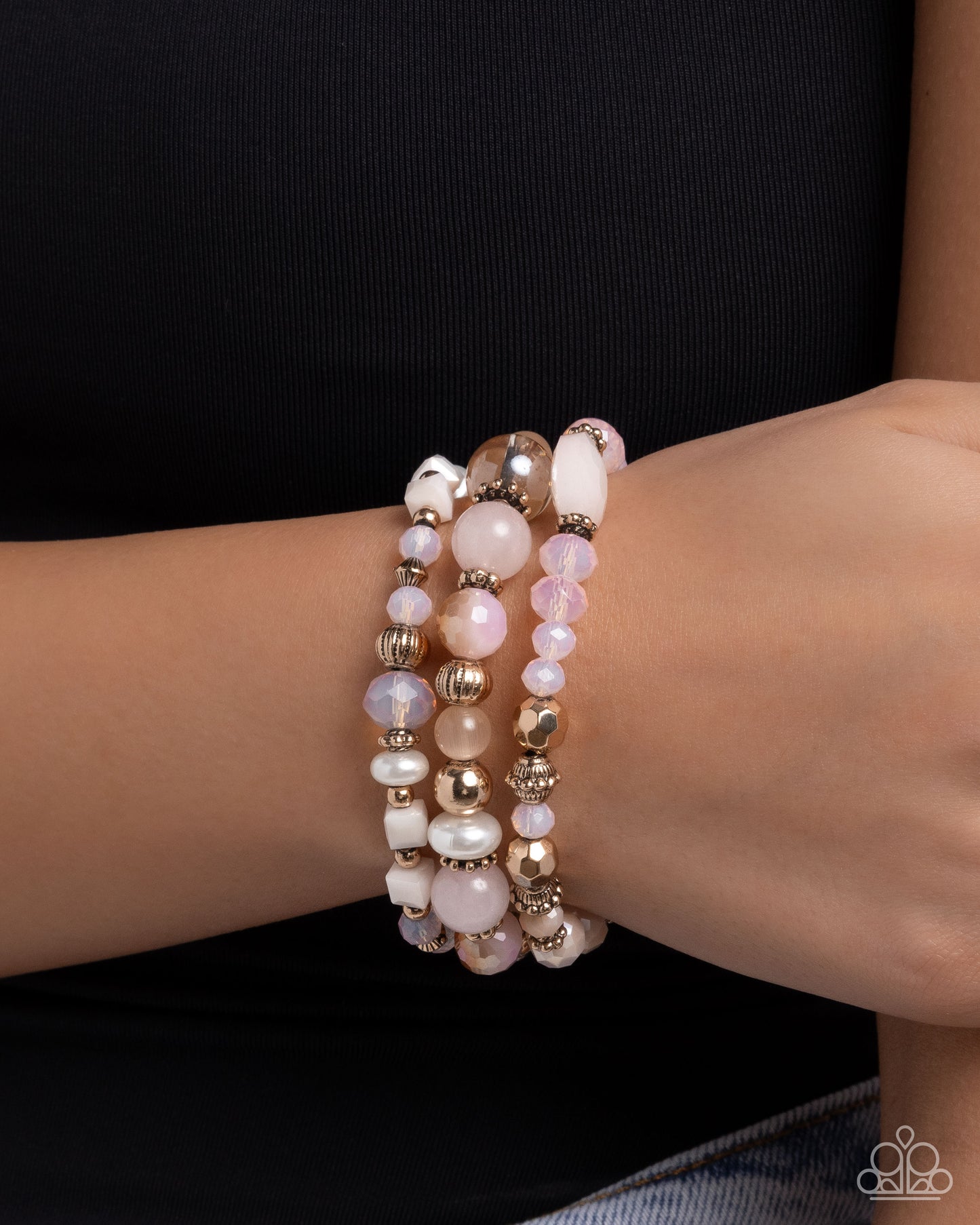 Stack of pearl and gold beaded bracelets on a wrist against a black background