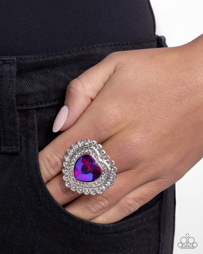 Hand wearing a purple heart-shaped ring with silver detailing against a black background
