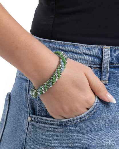Hand wearing a green beaded bracelet with blue jeans and black shirt