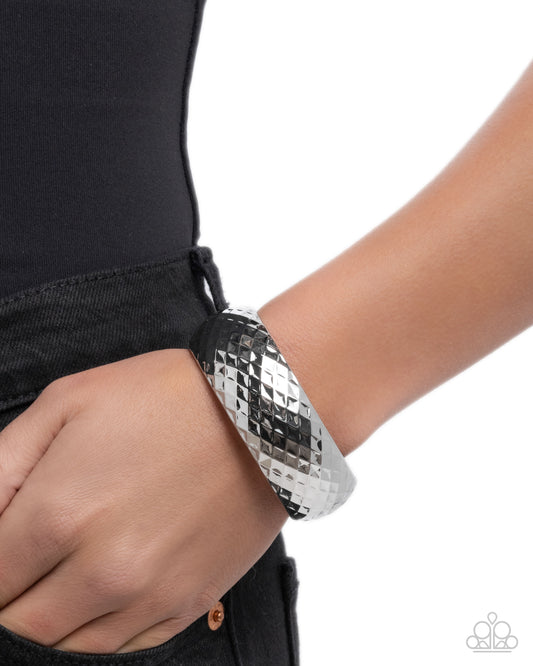 Silver textured bracelet on a wrist with a black background