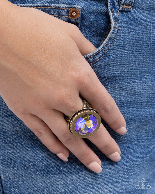 Hand wearing a decorative ring with a colorful gem on blue denim background