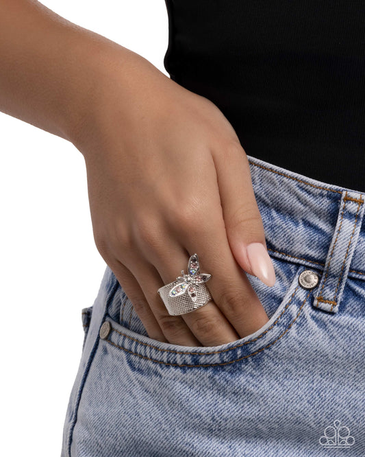 Hand wearing a silver ring with a heart and key design, inserted into a blue denim pocket.