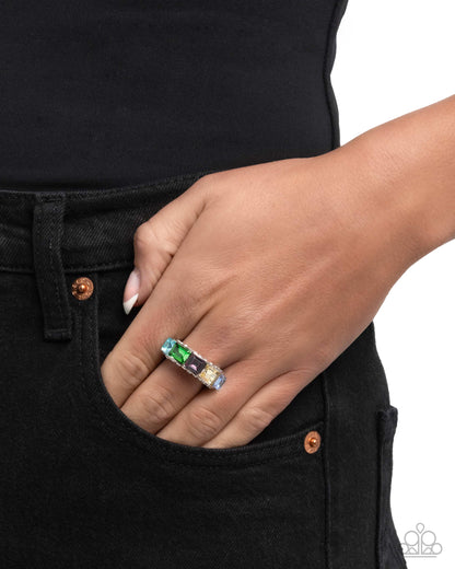 Hand wearing a ring with gemstones against a black background
