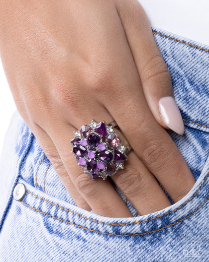 Hand wearing a decorative ring with purple gemstones against a denim background
