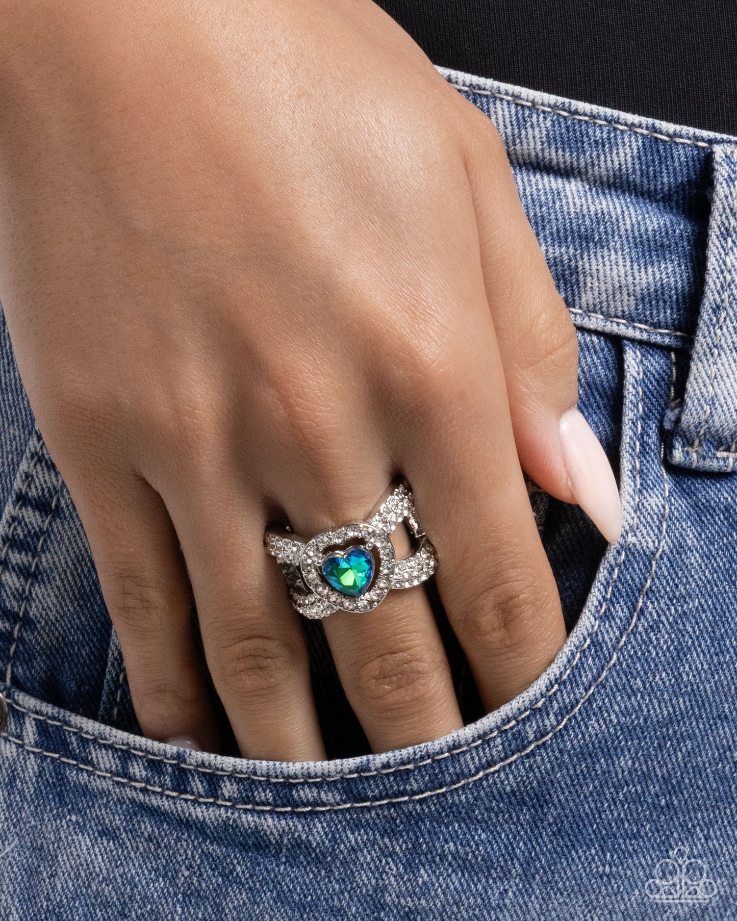 Hand wearing a ring with a heart-shaped gem, partially inserted into a pocket.