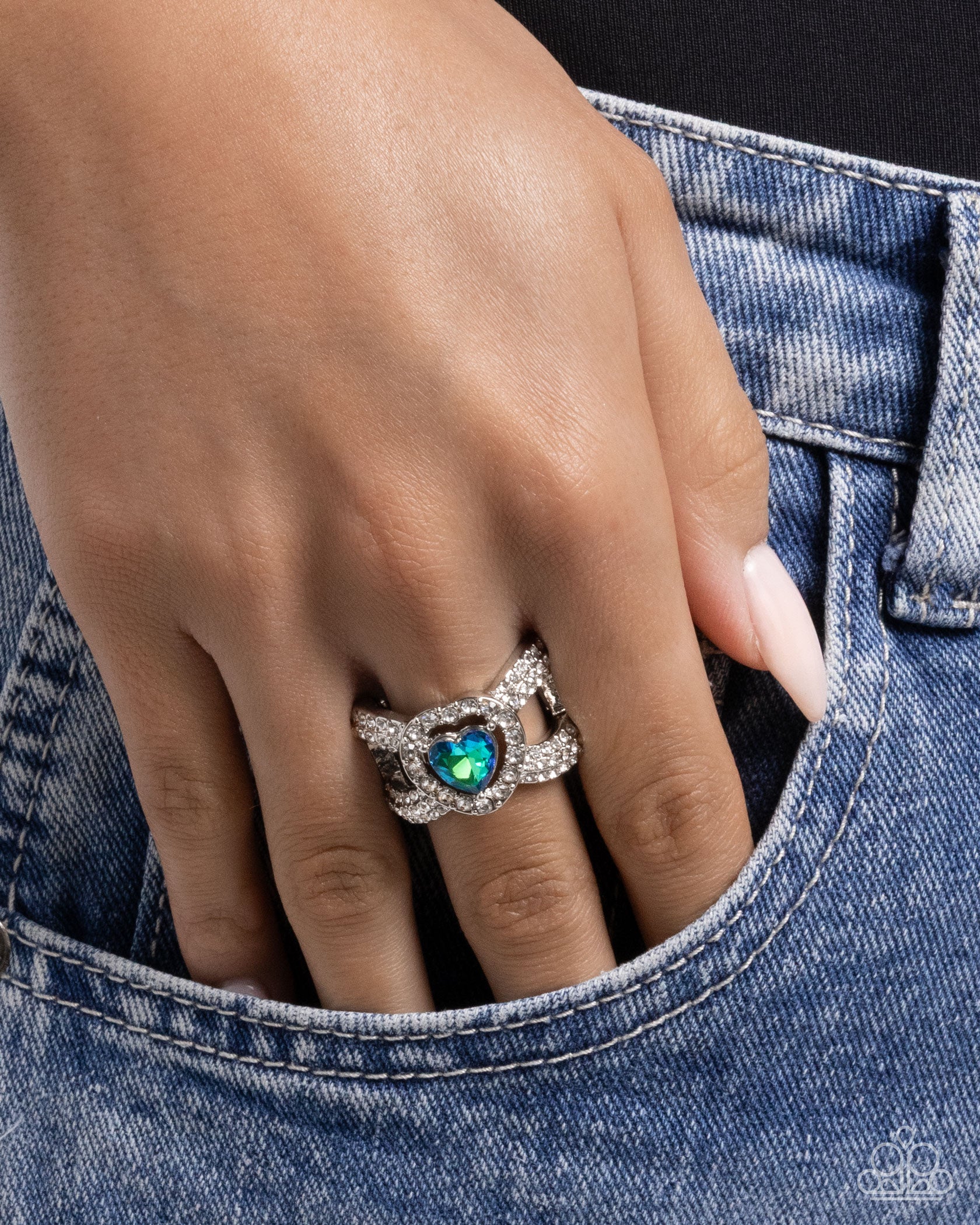 Hand wearing a ring with a heart-shaped gem, partially inserted into a pocket.