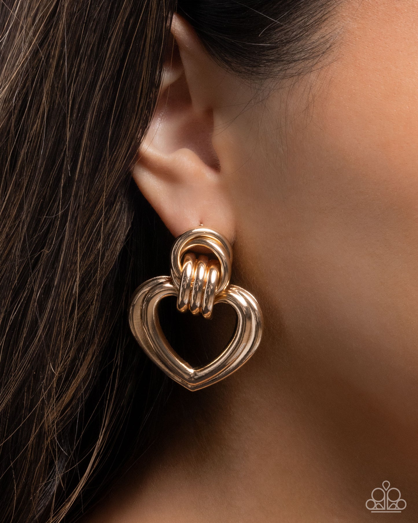 Gold heart-shaped earring worn on an ear with a blurred background
