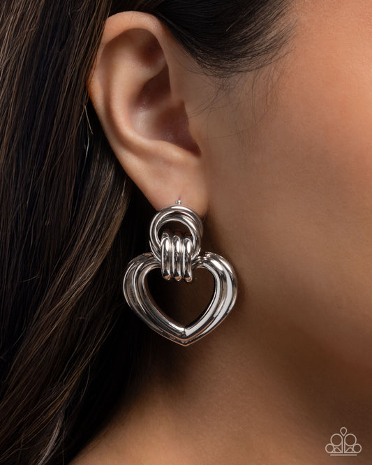 Silver heart-shaped earring worn by a person with dark hair.
