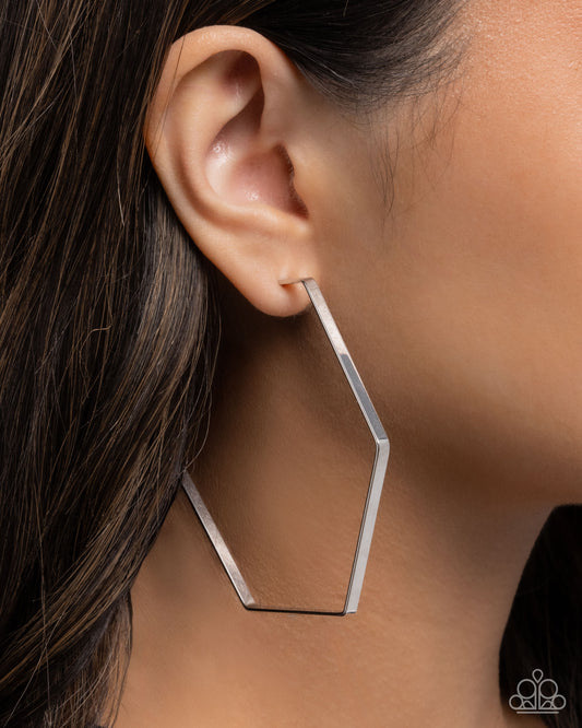 Silver geometric hoop earring worn by a person with dark hair.