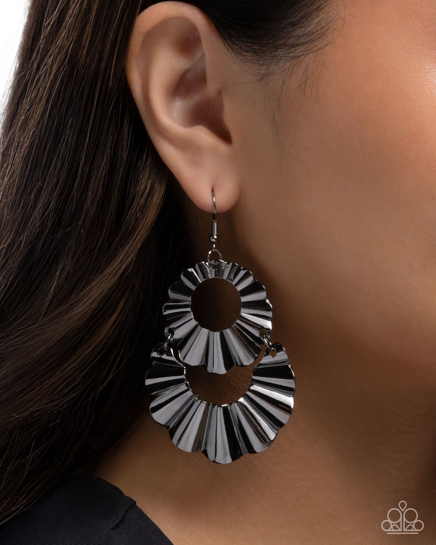 Silver and black circular earring worn by a person with dark hair.