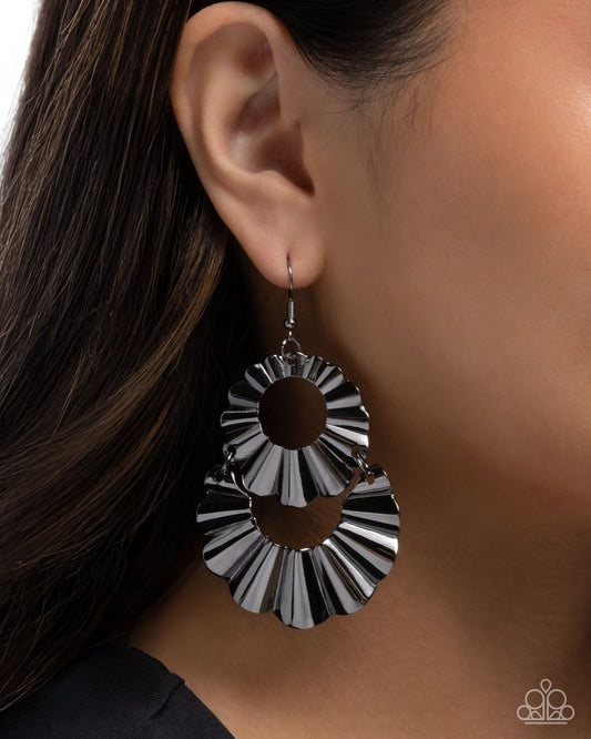 Silver and black circular earring worn by a person with dark hair.