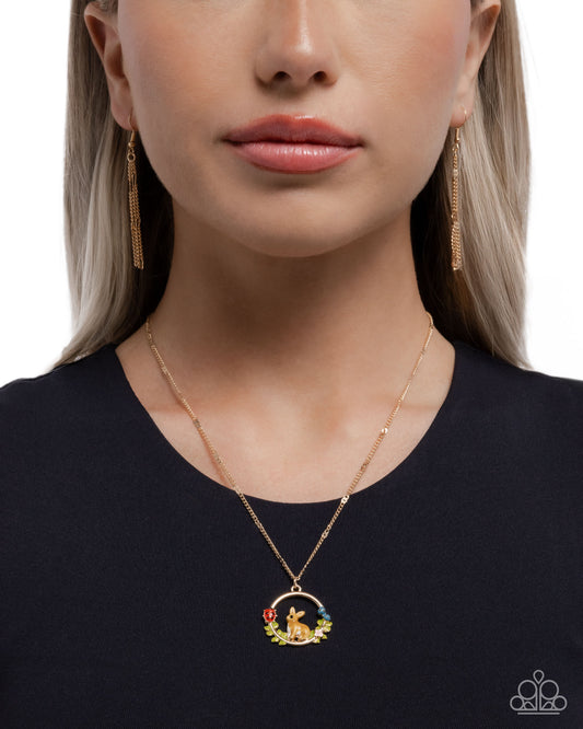 Woman wearing a gold necklace with a pendant, earrings, and a black top on a white background