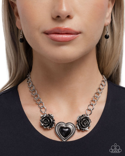 Necklace with black heart and rose designs worn by a model on a white background