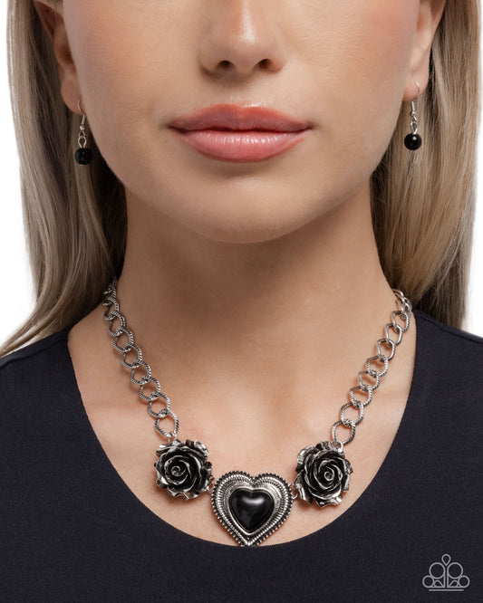 Necklace with black heart and rose designs worn by a model on a white background