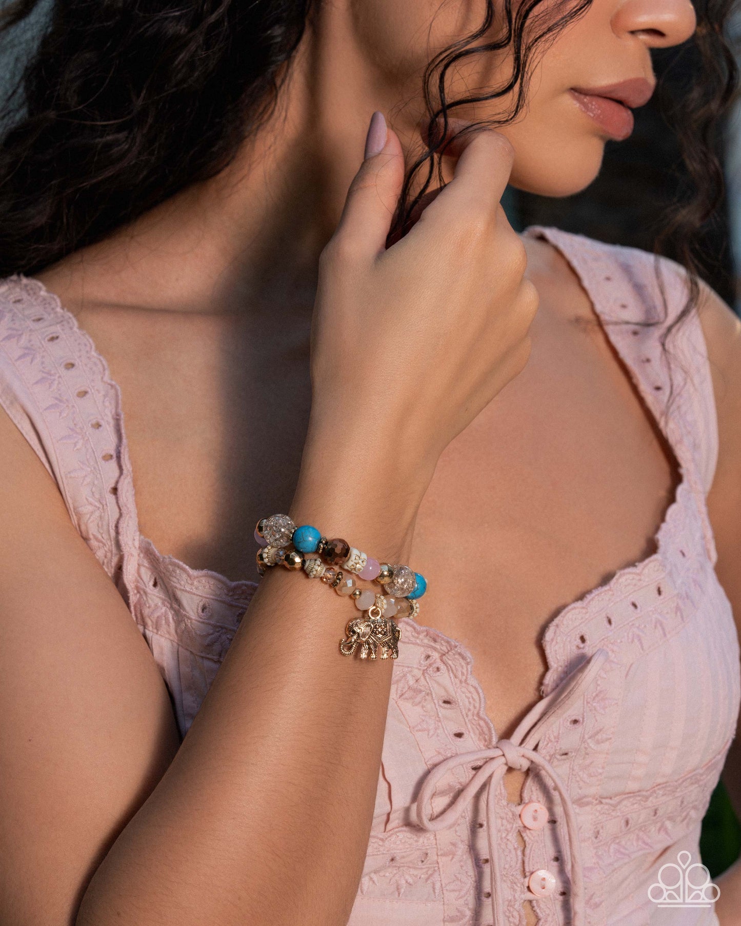 Woman wearing a pink lace top and a beaded bracelet with stones, touching her neck.