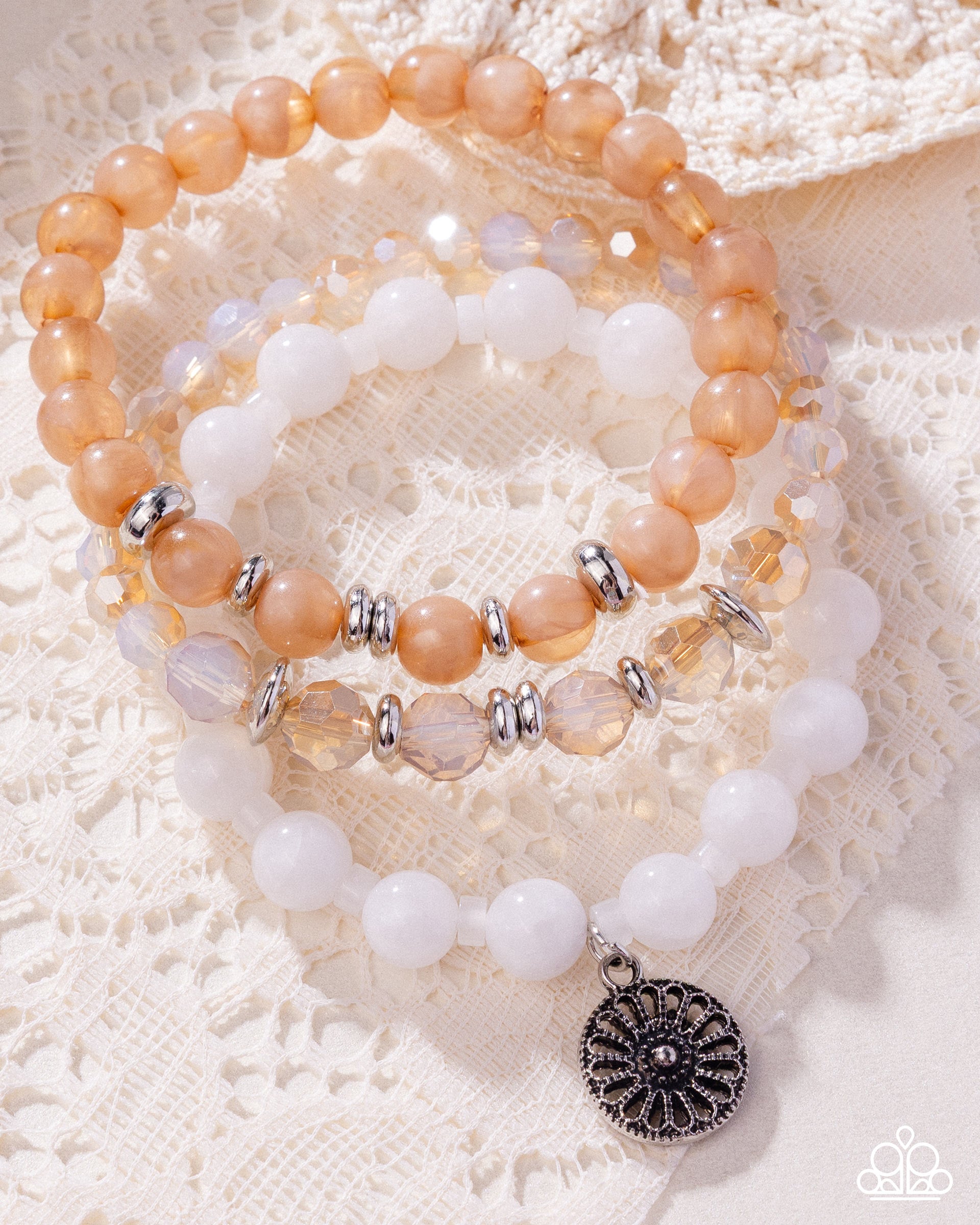 Stack of peach and white beaded bracelets with silver accents on a textured white surface