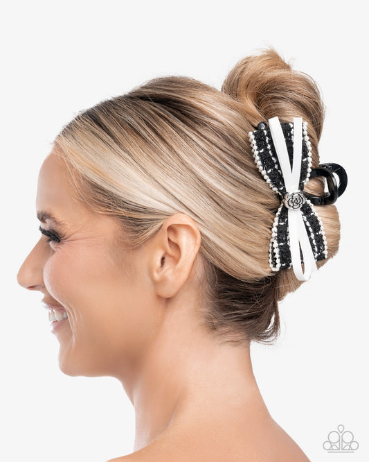 Woman with blonde hair styled in a bun with a decorative black and white bow accessory on a white background