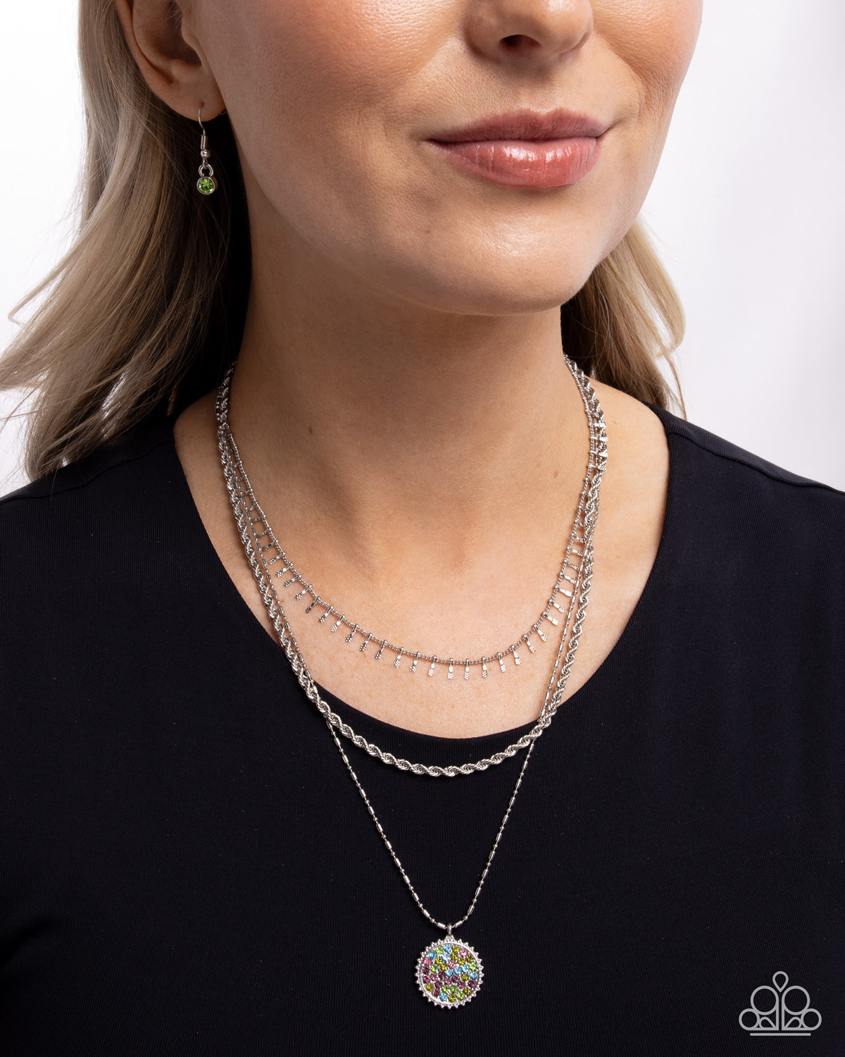Woman wearing multiple necklaces and earrings against a plain background