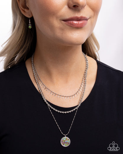 Woman wearing multiple necklaces and earrings against a plain background