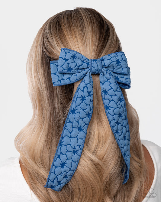 Blue floral-patterned hair bow on a person with blonde hair against a white background