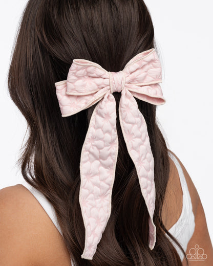 Pink textured hair bow in a person's hair on a white background