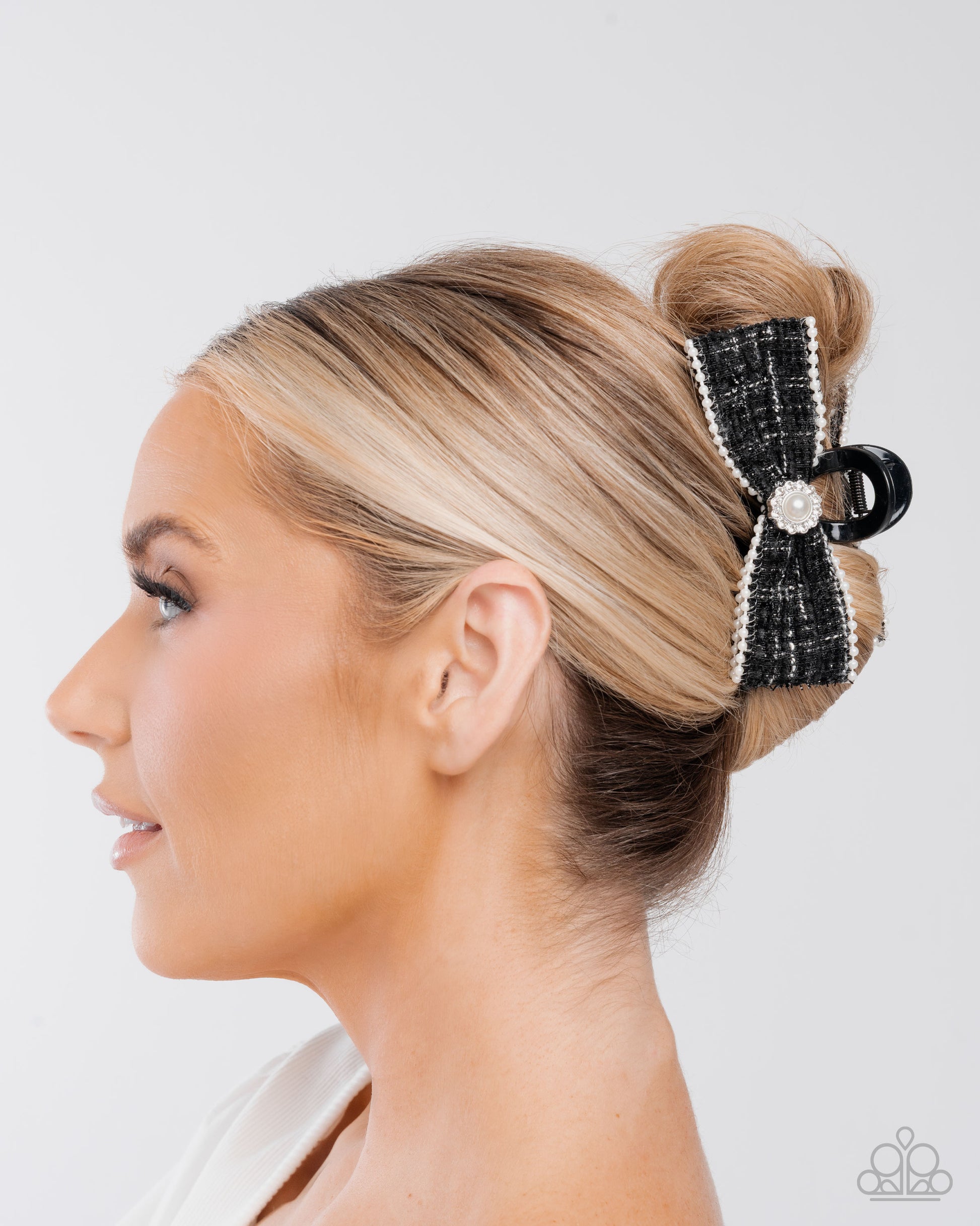 Woman with blonde hair styled in a bun with a decorative black hair clip against a white background