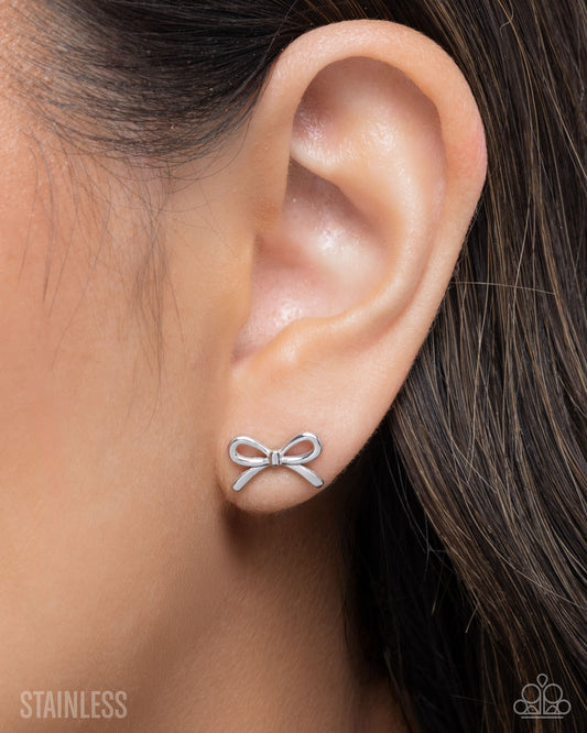 Silver bow-shaped earring worn on an ear with a blurred background