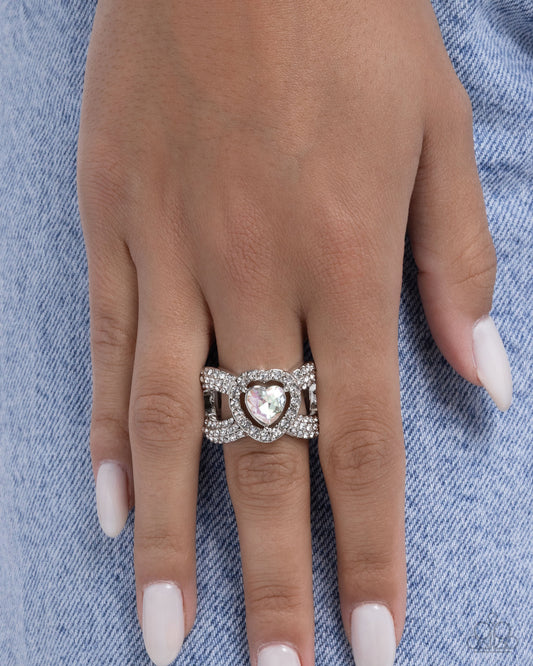 Silver ring with a heart-shaped gemstone on a hand against a denim background