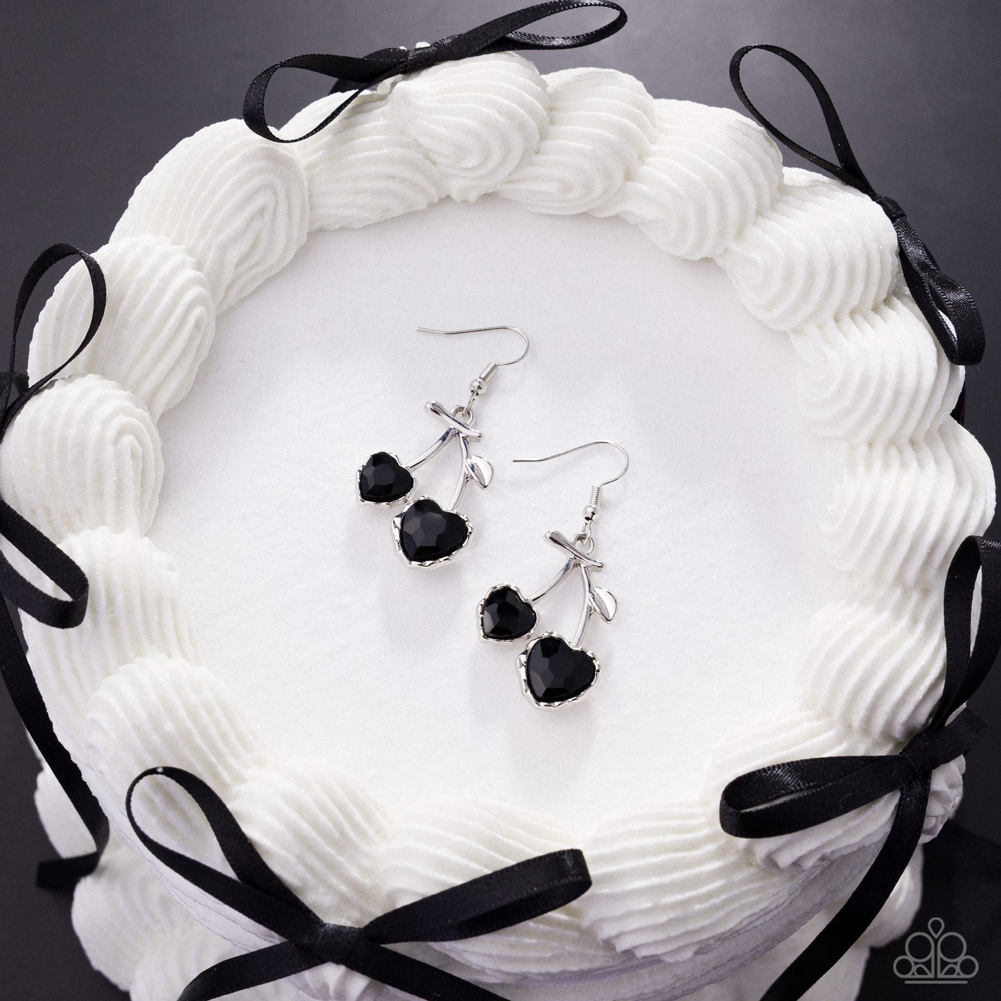 Black and silver earrings on a white textured surface with black ribbons.