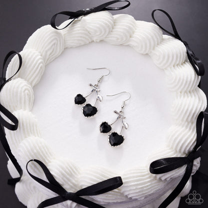 Black and silver earrings on a white textured surface with black ribbons.